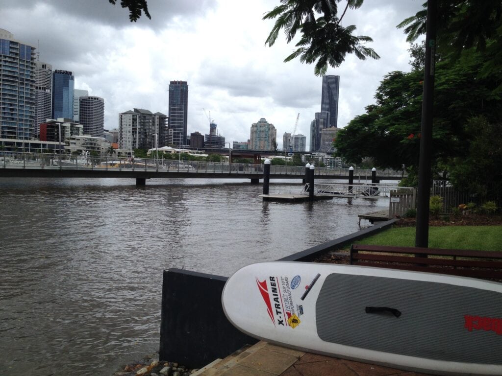 River boardwalk with standup paddleboard in foreground and city skyline in horizon at daytime