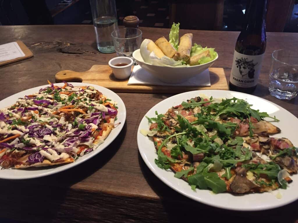 two pizzas on wooden bench with cider bottle