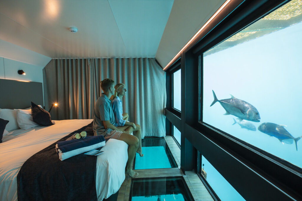 Couple sitting on the best of the reef suite underwater room, looking at the tropical fish