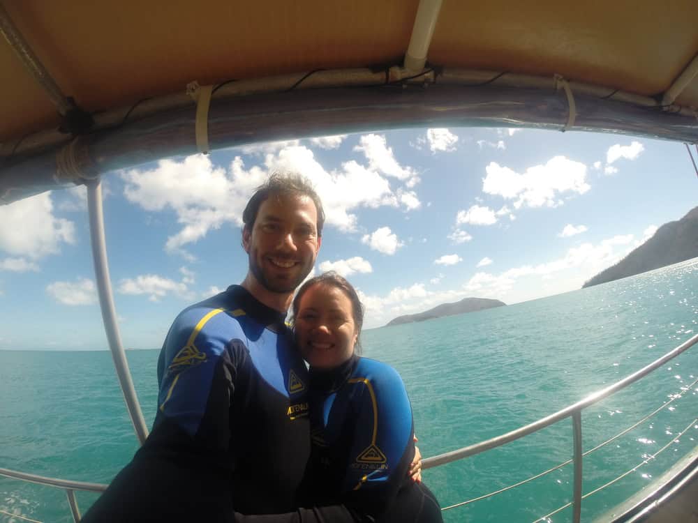 couple posing in wetsuits on a sailboat