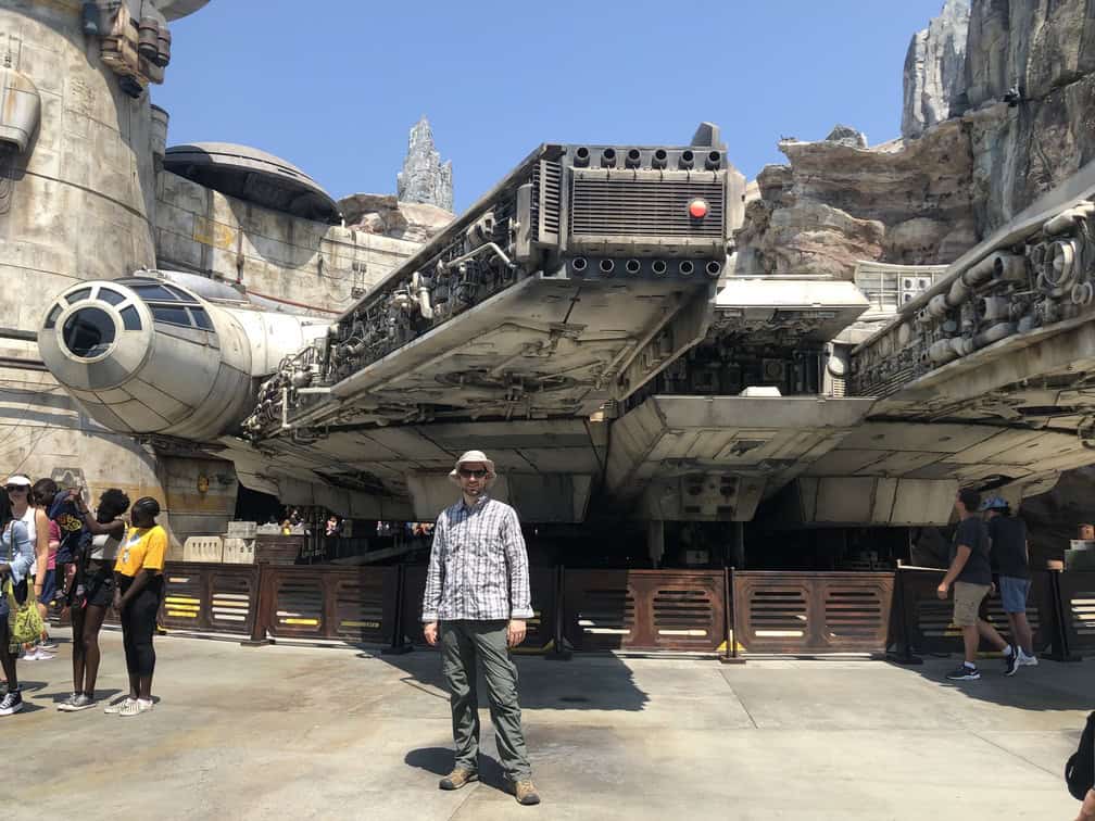man standing in front of life size model of millennium falcon from star wars at disney