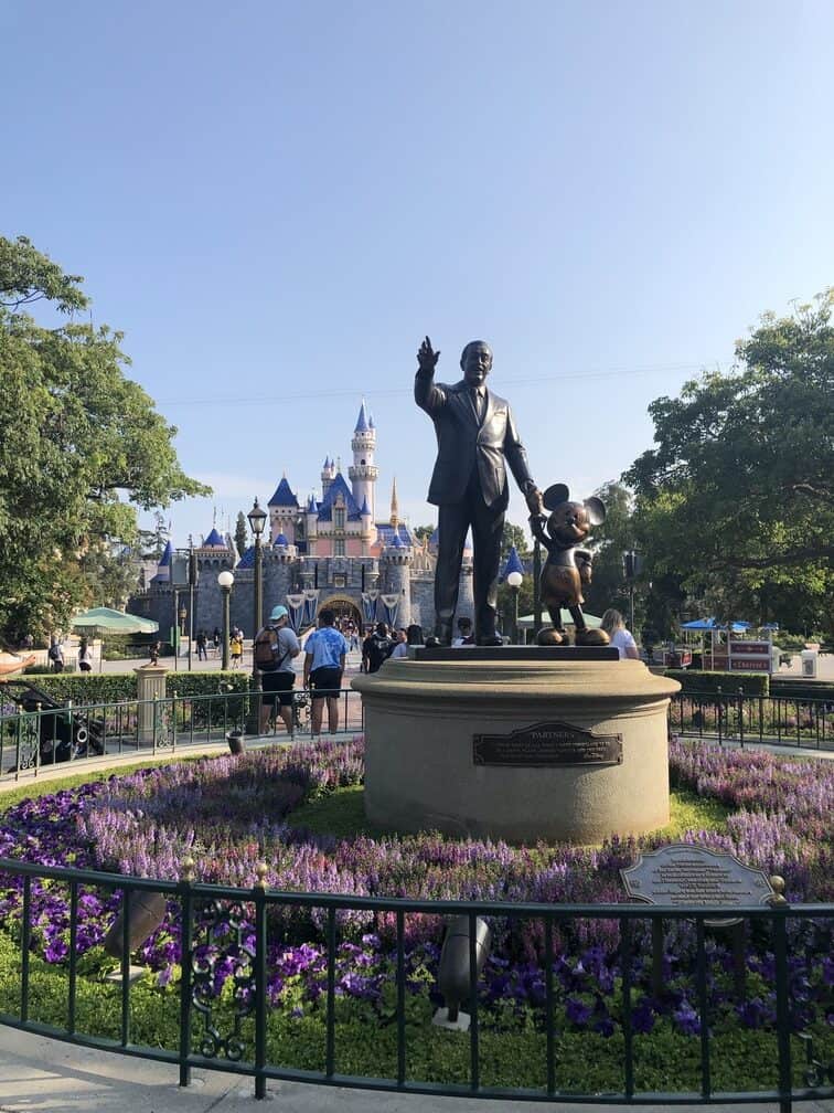 statue of walt disney and mickey mouse in circular garden with cinderella castle in background